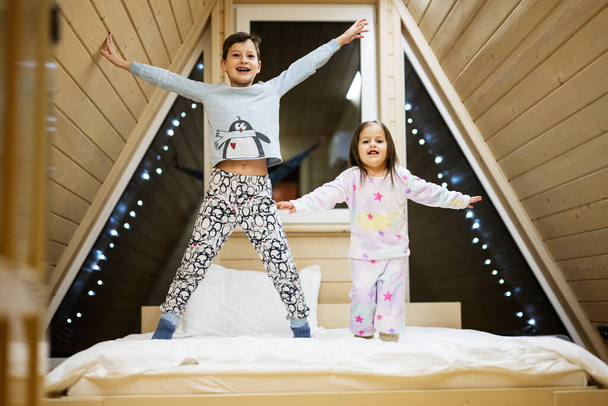 Children in soft warm pajamas playing at wooden cabin home. Concept of childhood, leisure activity, happiness. Brother and sister having fun and playing together.  - Foto, Imagem