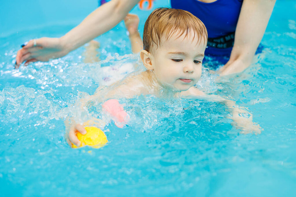 A 2-year-old little boy learns to swim in a pool with a coach. Swimming lessons for children - Fotoğraf, Görsel