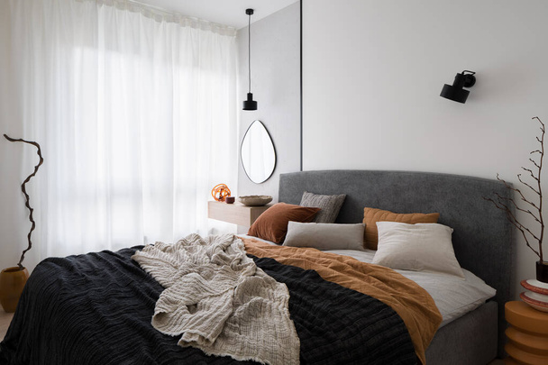 Cozy bed with stylish bedclothes in modern and bright bedroom with big window and trendy decorations - Photo, image