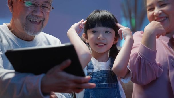 Little girl dancing with family at home, Cheerful granddaughter enjoying to listen and watch music video with grandparents, Senior grandparents having activities with grandchild at home happily - Photo, image
