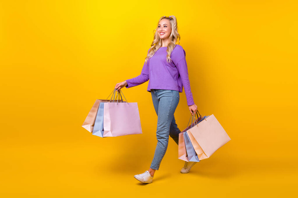 Full length photo of funny adorable lady dressed purple shirt walking holding bargains emtpy space isolated yellow color background. - Foto, Bild