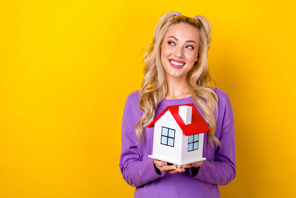 Photo of dreamy pretty lady dressed purple shirt rising little house looking emtpy space isolated yellow color background. - Foto, immagini