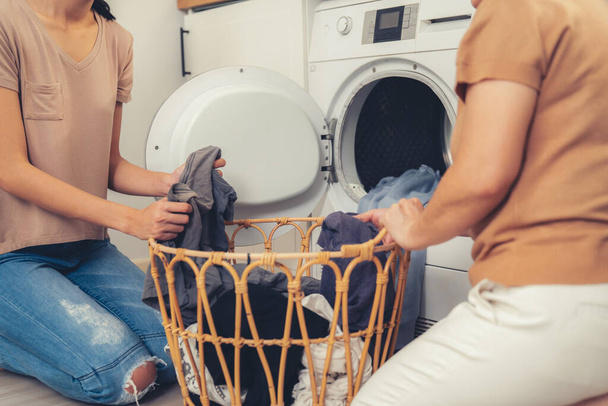 Daughter and mother working together to complete their household chores near the washing machine in a happy and contented manner. Mother and daughter doing the usual tasks in the house. - Photo, Image