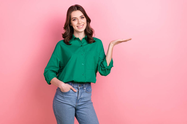 Portrait of gorgeous friendly girl curly hairstyle wear green shirt demonstrate proposition hand in pocket isolated on pink background. - Photo, image