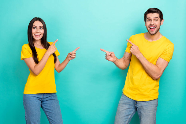 Photo of cheerful impressed married couple wear yellow t-shirts pointing fingers empty space isolated teal color background. - Foto, afbeelding