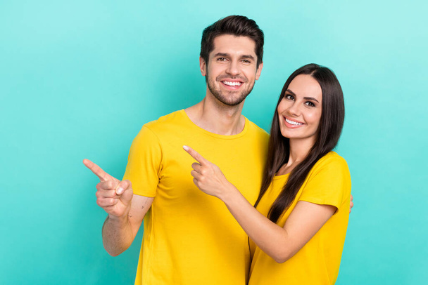Photo of cheerful satisfied promoters young family couple wear yellow t-shirts direct fingers mockup open new bar isolated on cyan color background. - Fotografie, Obrázek