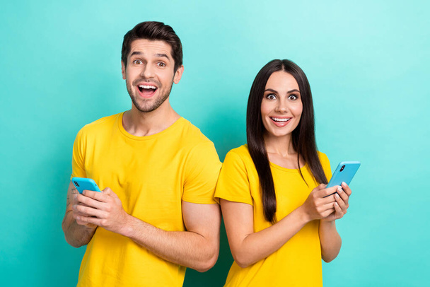 Photo of excited funny husband wife dressed yellow t-shirts typing messages modern gadget isolated turquoise color background. - Fotografie, Obrázek
