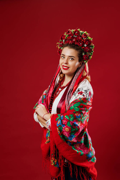 Portrait of ukrainian woman in traditional ethnic clothing and floral red wreath on viva magenta studio background. Ukrainian national embroidered dress call vyshyvanka. Pray for Ukraine - Foto, imagen