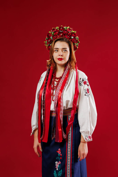 Портрет українки в традиційному етнічному одязі і квітковий червоний вінок на віві-пурпуровому фоні студії. Українська національна вишита сукня "Вишиванка". Молись за Україну - Фото, зображення