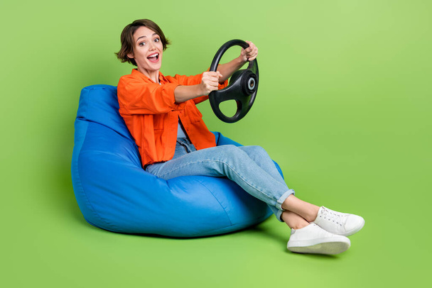 Full length photo of excited funny lady dressed jeans shirt bean bag driving auto empty space isolated green color background. - Foto, Bild