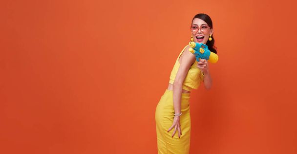 cheerful tourist woman traveling with water gun during Songkran festival studio on copy space orange background. - Photo, Image