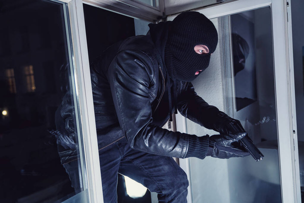 Burglar entering a victim's house with a gun at night - Zdjęcie, obraz
