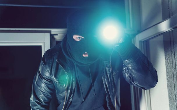 Inbreker probeert in te breken in een huis met een zaklamp - Foto, afbeelding