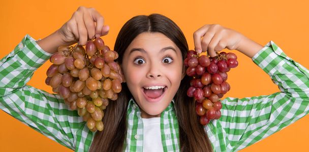 chocado adolescente niño con uvas racimo en amarillo fondo. - Foto, imagen