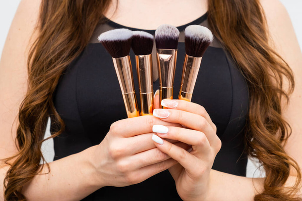 Close up in golden makeup brushes in woman hands with long hair.  - Foto, immagini