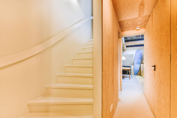 egy folyosó egy házban, fehér falak és világos fa lépcső vezet fel a második emeletre, van egy nyitott ajtó - Fotó, kép