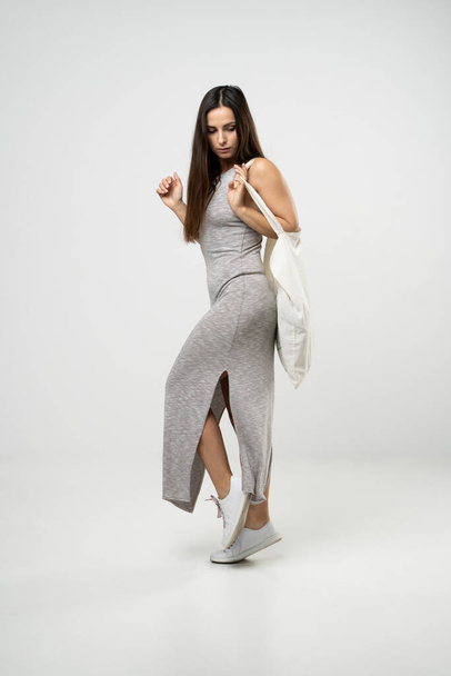 Happy young brunette woman in a grey dress dancing with a cotton bag with groceries. Zero waste concept. Eco friendly lifestyle. Mockup - Photo, Image