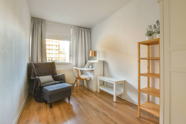 una sala de estar con una silla, escritorio y estantes en la pared frente a la puerta del dormitorio - Foto, Imagen
