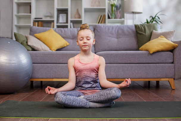 Little girl meditate sit at home. calm mindful child do yoga, breathing exercise, relax alone with closed eyes in lotus pose. - Фото, изображение