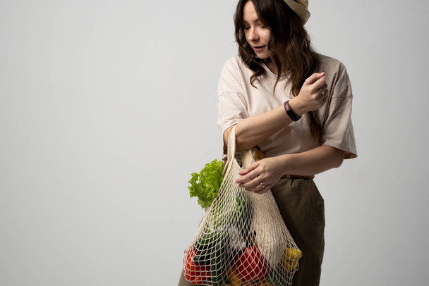 Brunette women in dress holds mesh bag with vegetables, fruits and groceries. Concept of no plastic. Zero waste, plastic free. Eco friendly concept. Sustainable lifestyle - Foto, Imagem