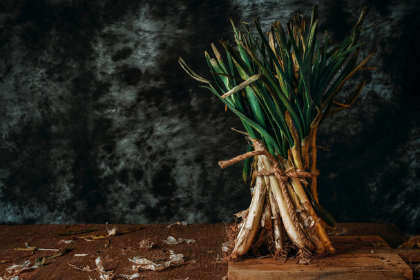 un ramo de calcetas crudas, las cebollas dulces típicas de Cataluña, España, de pie sobre una mesa de madera, sobre un fondo gris oscuro - Foto, Imagen