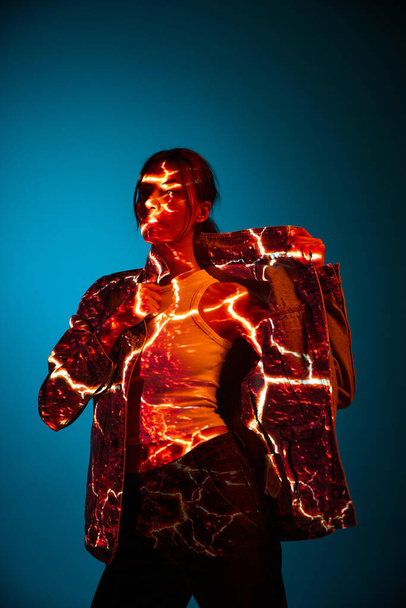 Elektrische lampen. Futuristische stijl portret van jonge vrouw met digitale neon filter lichten op kleding over donkerblauwe achtergrond. Concept van kunst, mode, cyberpunk, futurisme en creativiteit. - Foto, afbeelding
