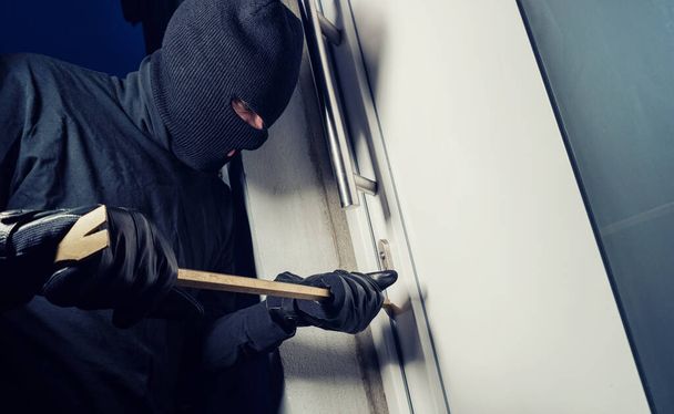 Burglar in a mask breaking Into a house with a crowbar - Fotoğraf, Görsel