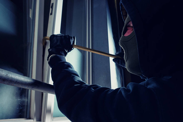 ladrón usando palanca para irrumpir en la casa de una víctima por la noche  - Foto, Imagen