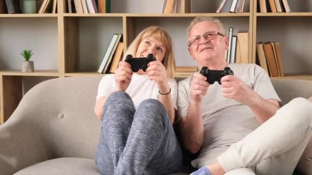 Onnellinen eläkkeellä pari pelaa pelejä joystick. Vanhempi pari, kiehtoo auton ajopeli, istuu sohvalla kotonaan edessä televisioruudulla. Eläkeläisten onnellinen elämä - Materiaali, video