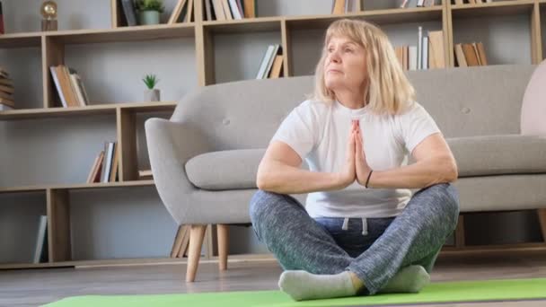Amerikanische Großmutter macht Yoga-Übungen zu Hause im Wohnzimmer. Ältere Frau während der Morgenmeditation - Filmmaterial, Video
