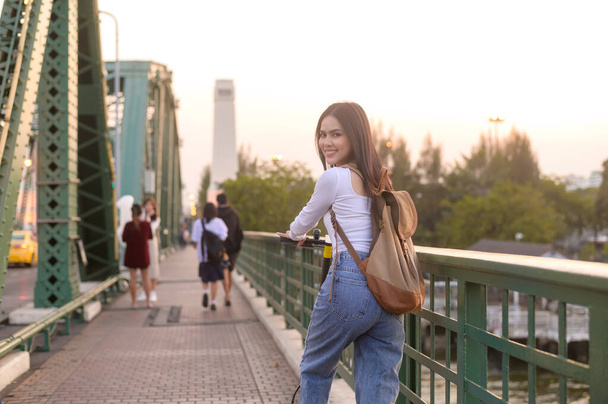 Portrait of young beautiful woman with an electric scooter  over bridge in modern city  background - Foto, afbeelding