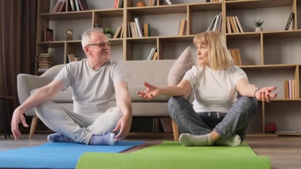 Starý krásný pár dělá jógu cvičení sedí na fitness rohože v obývacím pokoji. Zdravý životní styl v důchodu - Záběry, video
