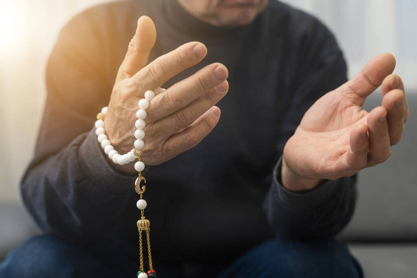 an elderly man prays with a rosary and the flag of the United Arab Emirates. - Foto, Bild