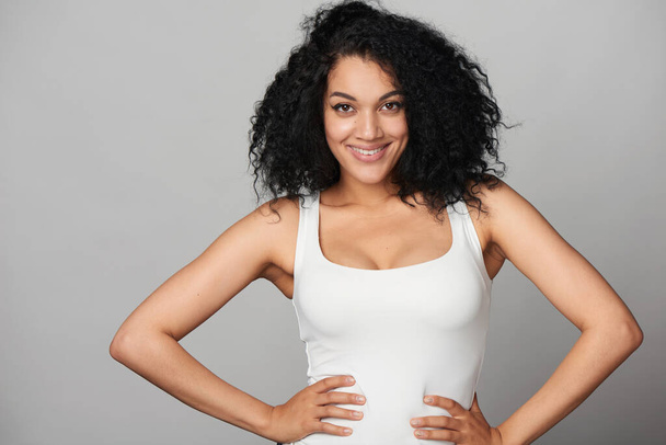 Happy smiling mixed race girl with hands on hips, on grey background, front view - Foto, Imagen