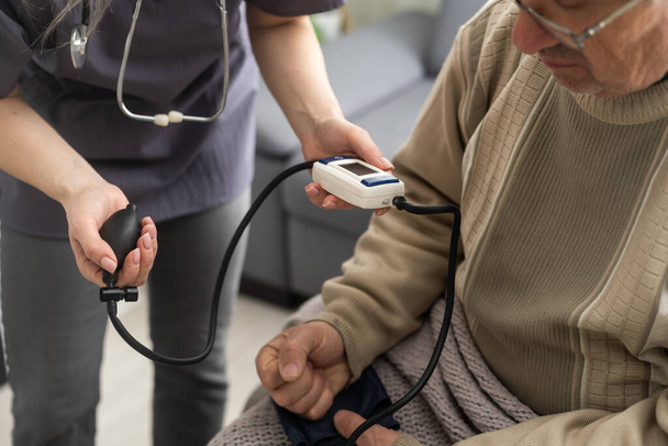 Nurse measure high blood pressure of a sick senior mature male patient in medical clinic closeup. Doctor checking arterial blood pressure of elderly man with hypertension. Healthcare concept. - Photo, Image