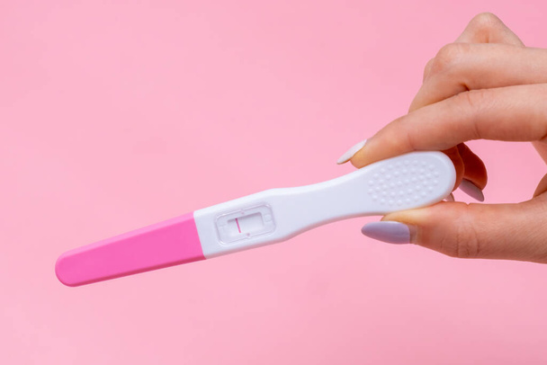 Womans hand holding negative pregnancy test with one stripe on pink background with copy space. - Photo, image