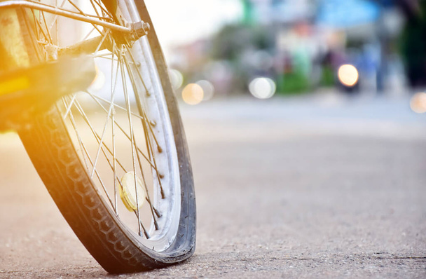 Roda traseira da bicicleta que é plana e estacionada no pavimento ao lado da estrada, lente flare editado. - Foto, Imagem