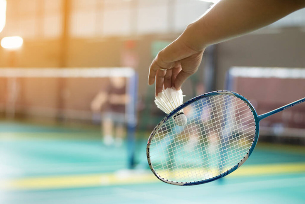 Badminton giocatore tiene racchetta e bianco navetta crema davanti alla rete prima di servirlo ad un altro lato del campo. - Foto, immagini