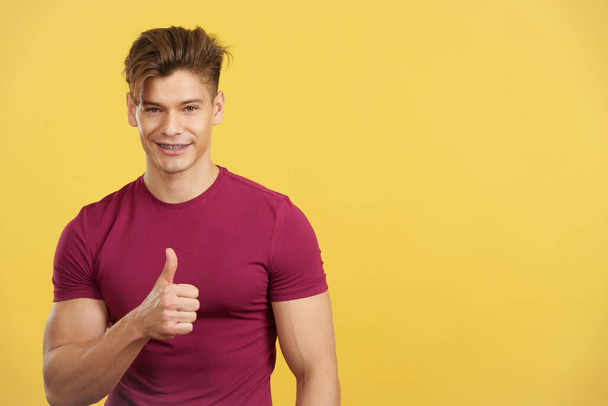 Strong man gesturing approval with the thumb up in studio with yellow background - Foto, Bild