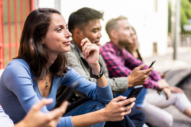 大学の裏庭に座っているスマートフォンを使用して普及した友人グループ-若い人たちは、携帯電話で中毒-常に接続された学生と技術悲しい生活の概念-鮮やかなフィルター - 写真・画像