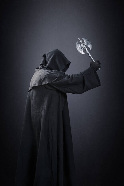 Figure in hooded cloak with axe over dark misty background - 写真・画像