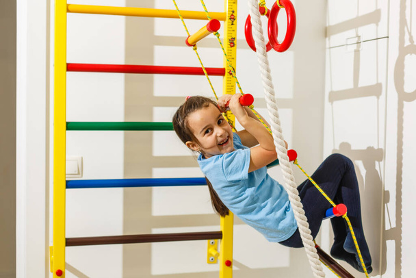 Portrait of a happy child in a gaming entertainment center. The sweating little girl hanging on a soft horizontal bar. A beautiful active baby goes in for sports. - Foto, Bild