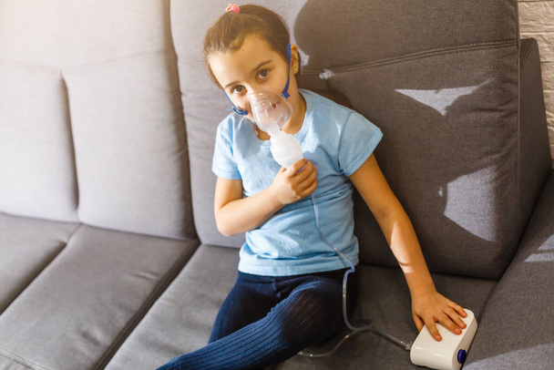 A kis kaukázusi lány speciális maszkkal lélegzik, ami segít megállítani az asztmás rohamot vagy enyhíteni a légúti betegség tüneteit.. - Fotó, kép