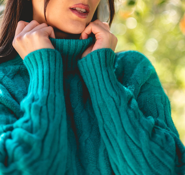 Крупный план девушки с красивыми руками, темными ногтями и зеленым свитером (с деталями ткани) в солнечном парке - Фото, изображение