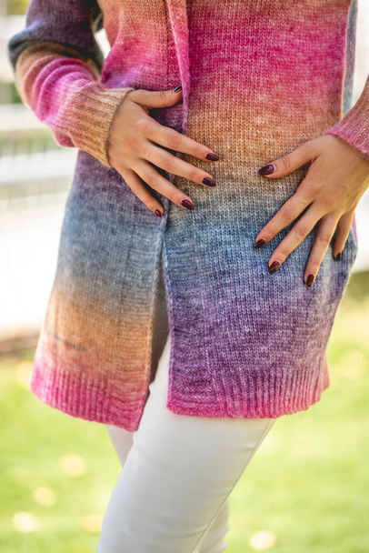 Primo piano della ragazza con belle mani, unghie scure e maglione arcobaleno colorato (con dettagli in tessuto) nel parco soleggiato - Foto, immagini