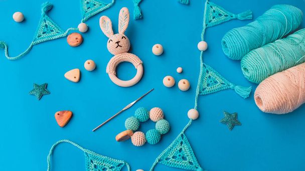 Layout of crochet baby toys, crochet hook and skeins of yarn on bright blue surface. Crochet for babies. - Photo, Image