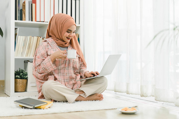 A beautiful young Muslim woman wearing casual clothing is working on a laptop computer - Fotografie, Obrázek