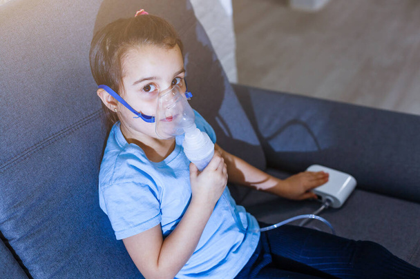 Pieni valkoihoinen tyttö hengittää erityisellä maskilla, joka auttaa pysäyttämään astmakohtauksen tai lievittämään hengitystiesairauden oireita.. - Valokuva, kuva