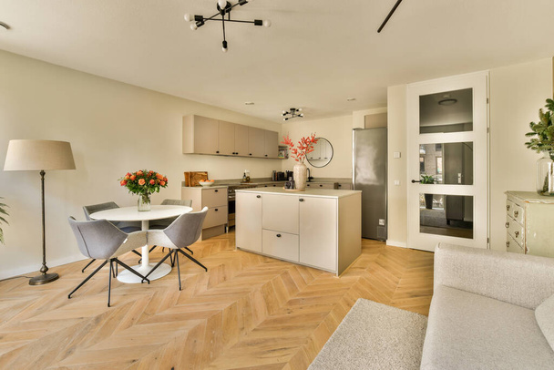 a living room with wood flooring and white furniture in the center of the room is an open kitchen area - Photo, Image
