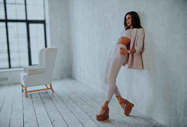 Young business style woman standing at the wall in soft white interior - Foto, afbeelding